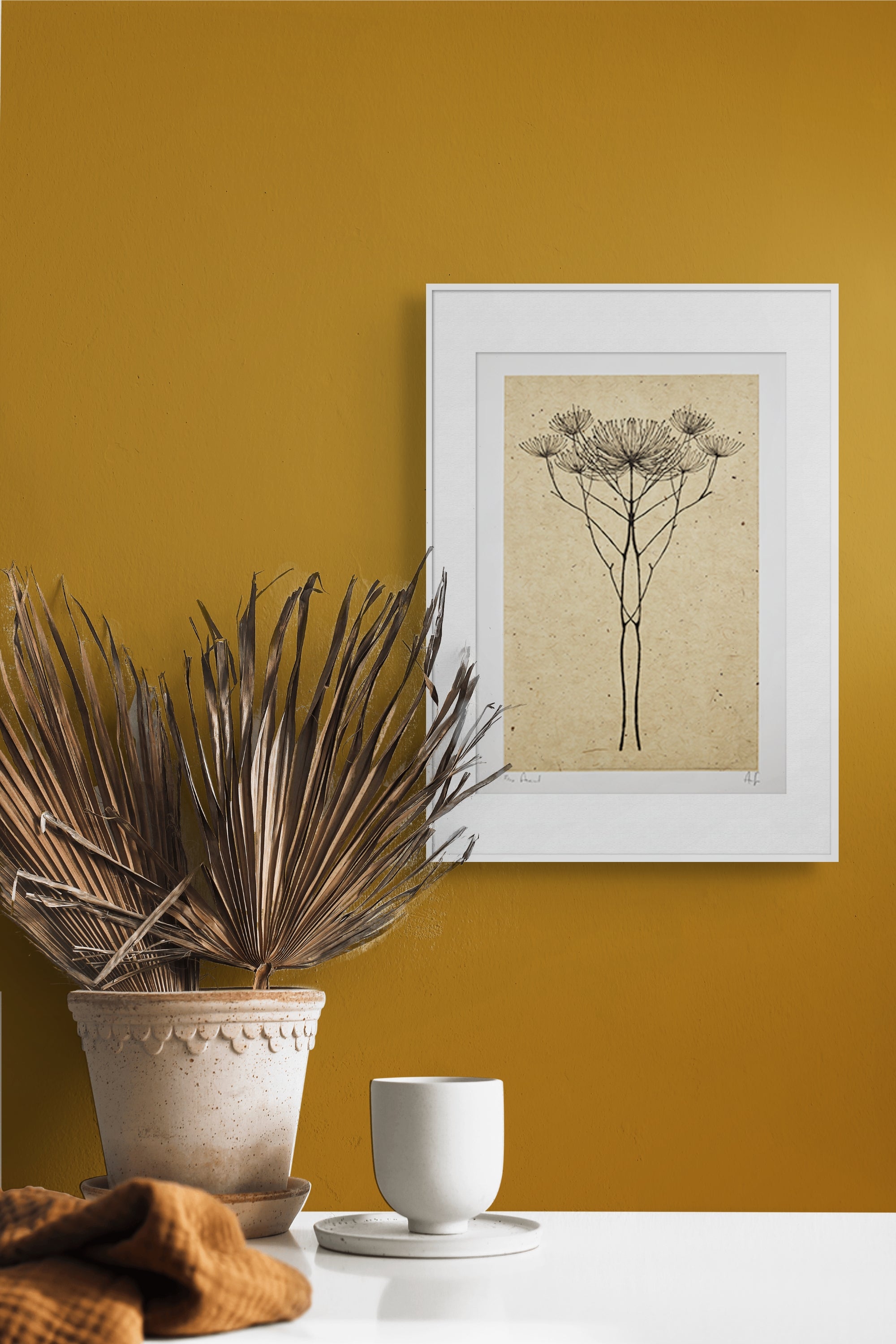 Gerahmte Kaltnadel-Radierung "Axial" von Anna Francis – Weiß gerahmter Druck mit Doldenblüte an senfgelber Wand neben Tontopf mit getrockneten Palm.