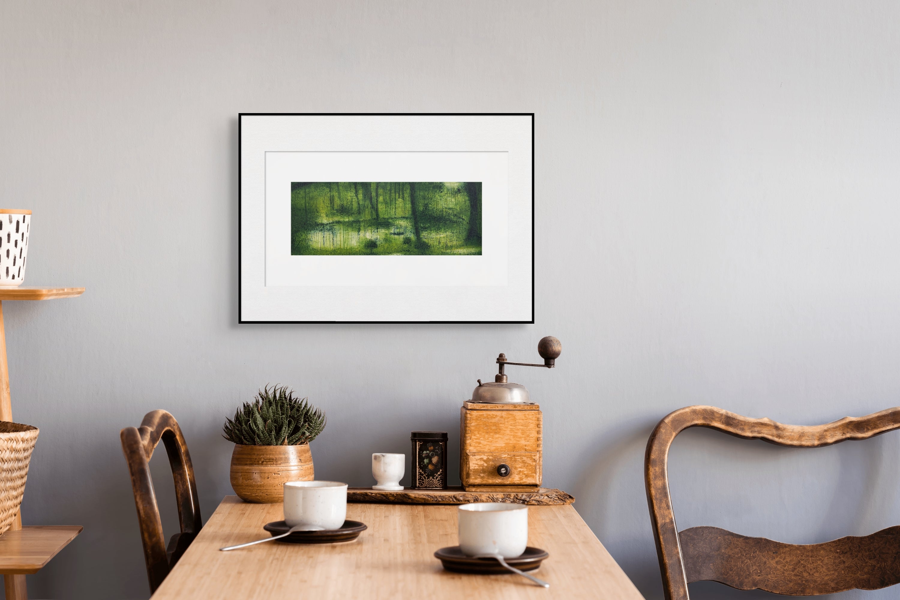 Gerahmte Radierung "Saihoji" von Stephen Lawlor – Gerahmtes Querformatbild an heller Wand über Holztisch mit Stühlen, Kaffeemühle und Topfpflan.