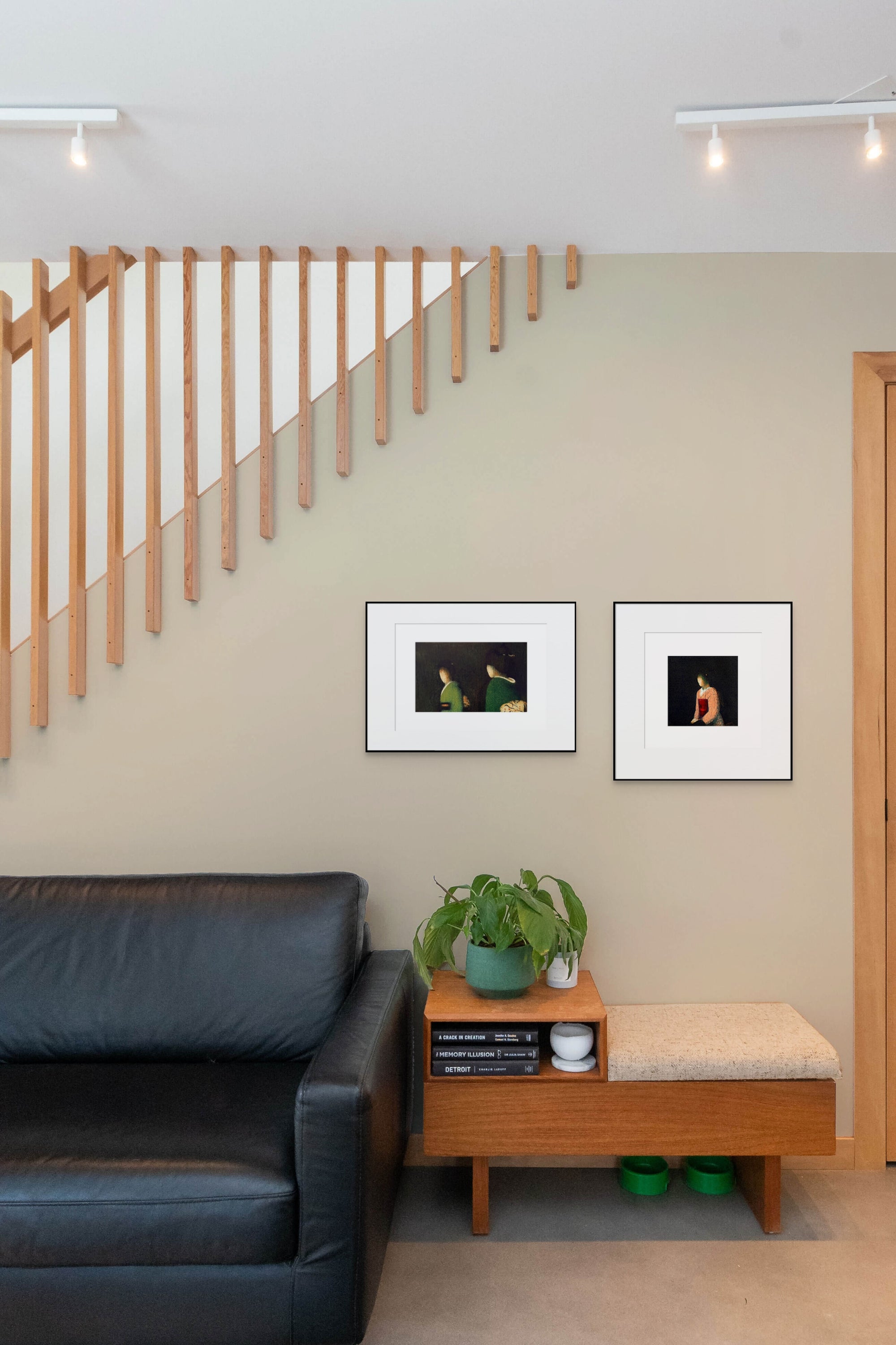 Gerahmte Radierung "Kawako" von Stephen Lawlor – Mockup: zwei gerahmte Figuren-Bilder an heller Wand neben Holztreppe, schwarzes Sofa und Beistell.