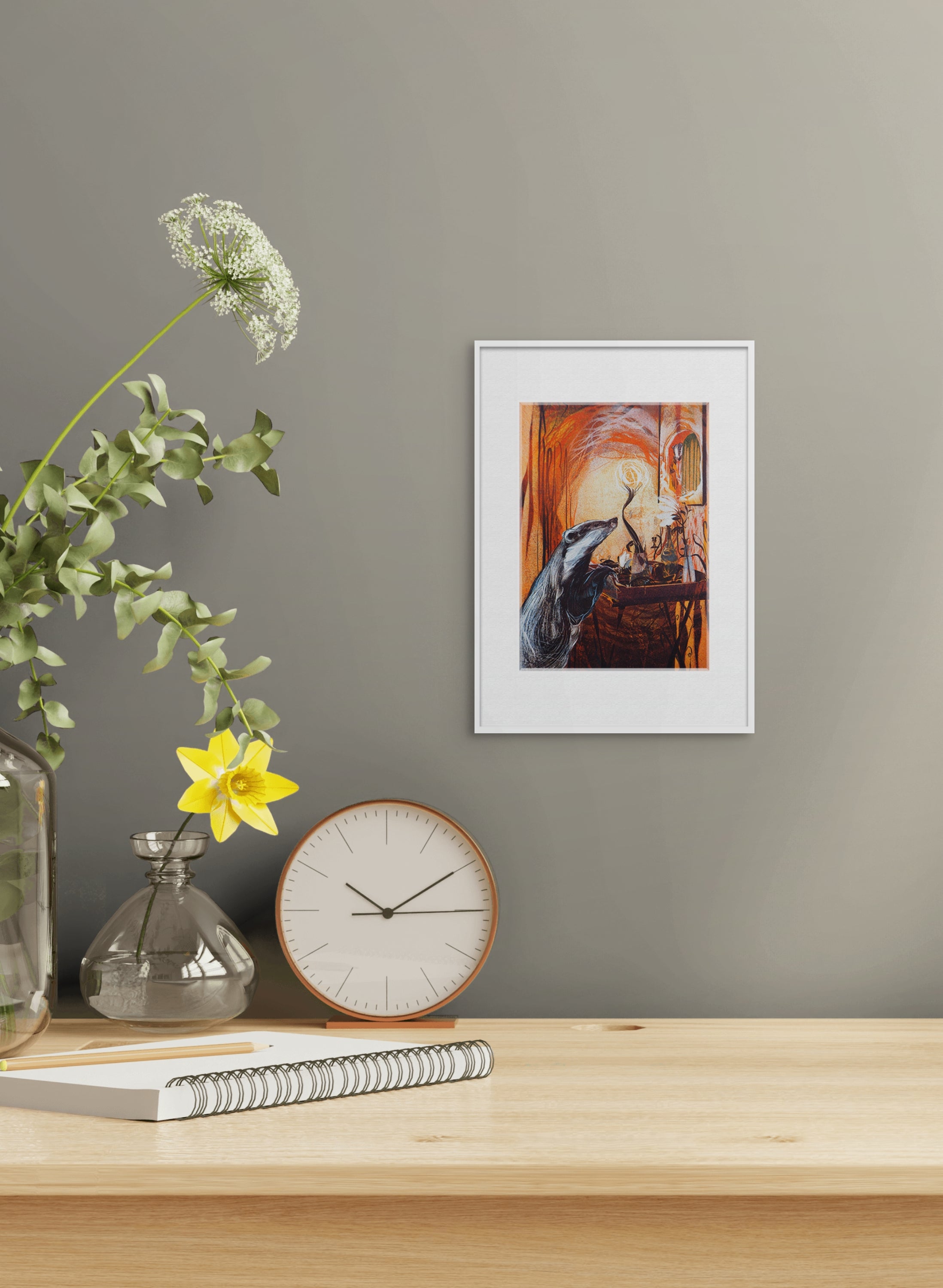 Gerahmte Risografie "Badger in the Willows" von Georgia Green – Weiß gerahmter farbiger Druck mit Dachs an grauer Wand über Holztisch mit Uhr, Vase.