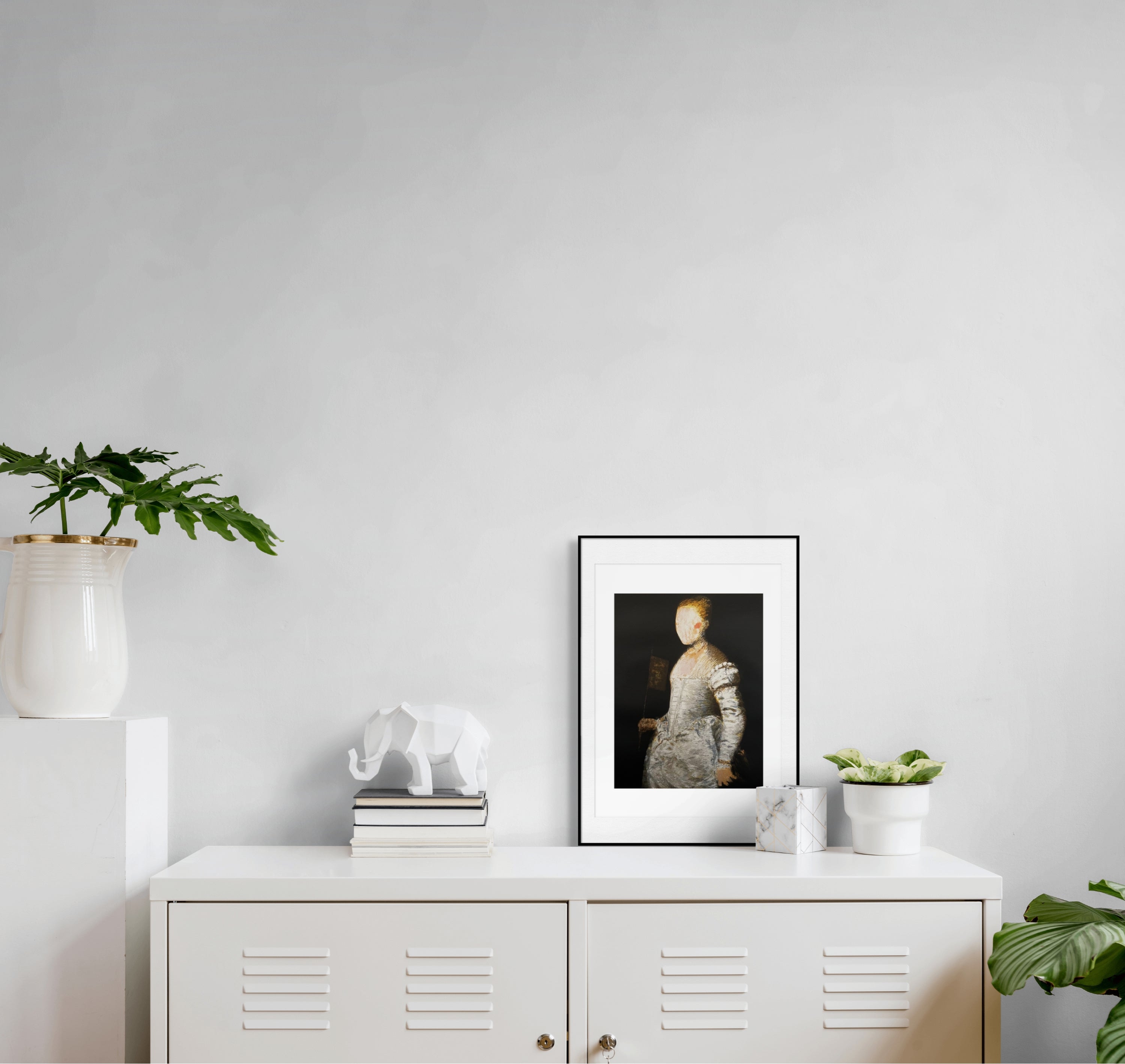 Gerahmte Siebdruck "Lavinia" von Stephen Lawlor – Gerahmtes Bild auf weißer Metallkommode neben Bücherstapel mit Elefantenfigur und Topfpflanzen.